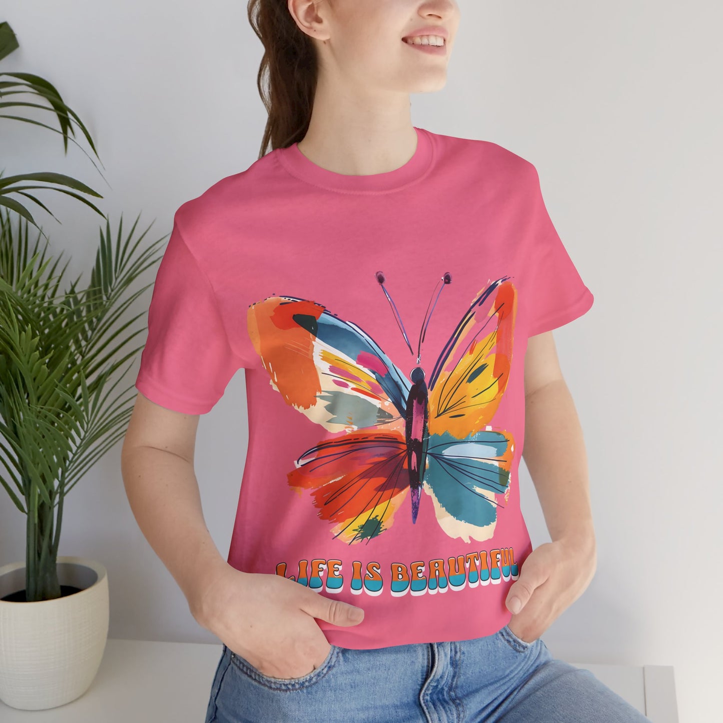 Colorful cartoon-style butterfly with vibrant wings and the text 'Life is Beautiful' designed for t-shirts in colors including Aqua, Athletic Heather, Berry, Black, Dark Grey Heather, Heather Red, Heather Team Purple, Heather True Royal, White, and Charity Pink