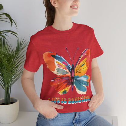 Colorful cartoon-style butterfly with vibrant wings and the text 'Life is Beautiful' designed for t-shirts in colors including Aqua, Athletic Heather, Berry, Black, Dark Grey Heather, Heather Red, Heather Team Purple, Heather True Royal, White, and Charity Pink