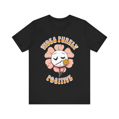 Cute pink flower with a smiling face and a yellow flower in its mouth, accompanied by the text "Vibes Purely Positive." This cheerful design is perfect for t-shirts available in colors Aqua, Berry, Black, Dark Gray, Heather Kelly, Heather Team Purple, Heather True Royal, Navy, White, and Charity Pink.