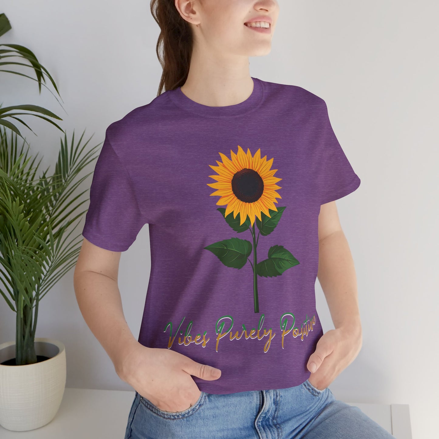 Sunflower illustration with 'Vibes Purely Positive' phrase - a vibrant sunflower with yellow petals and dark brown center, green leaves on a stem, conveying a positive message printed in t-shirts of different colors like "Army Athletic Heather Berry Black Heather Navy Heather Team Purple Navy White Ash Heather Aqua"