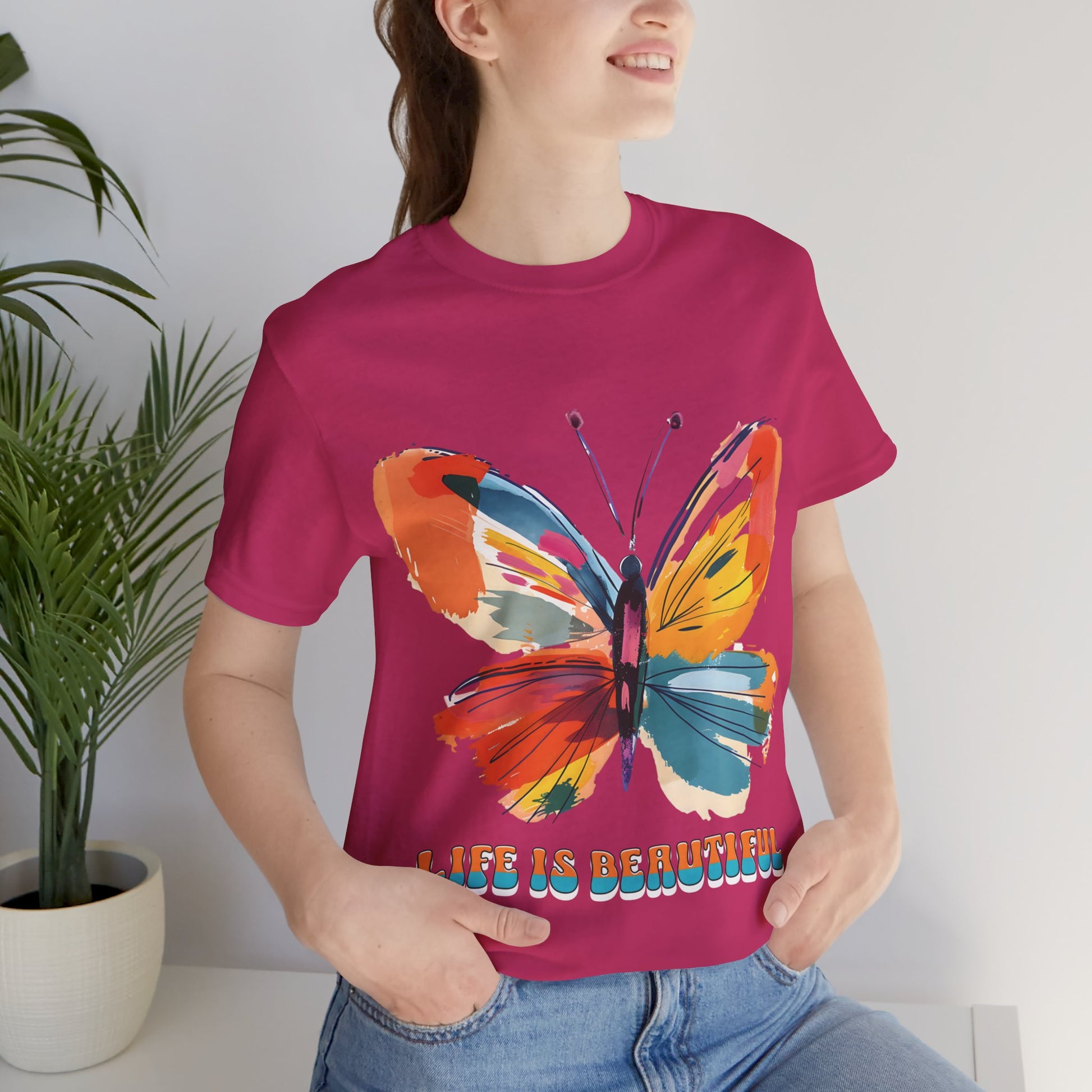 Colorful cartoon-style butterfly with vibrant wings and the text 'Life is Beautiful' designed for t-shirts in colors including Aqua, Athletic Heather, Berry, Black, Dark Grey Heather, Heather Red, Heather Team Purple, Heather True Royal, White, and Charity Pink