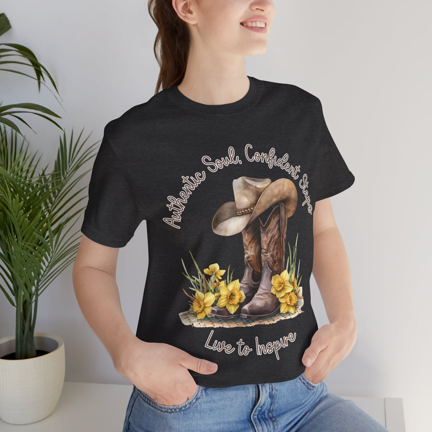 Brown leather cowboy boots with detailed stitching and a light brown hat on top, surrounded by green leaves and yellow flowers, with inspirational phrases ‘Authentic Soul,’ ‘Confident Steps,’ and ‘Live to Inspire’ written above and below on a white background colors tshirt Aqua Athletic Heather Baby Blue Black Dark Grey Heather Heather Kelly Heather Red Heather Team Purple Heather True Royal Navy Pink White Heather Aqua Heather Mauve Charity Pink.