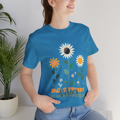 Colorful floral illustration with 'Positive Vibes' - featuring a trio of vibrant flowers, including a sunflower-like bloom with white petals, an orange flower with simple petals, and a yellow flower with round petals, all set against a light backdrop adorned with whimsical dots and the uplifting phrase 'Positive Vibes' in playful orange font, Aqua, Athletic Heather, Berry, Black, Dark Grey, Dark, Grey, Heather, Heather Kelly, Heather Red, Heather Team, Purple, Navy, Pink, Ash, Heather, Aqua, Charity Pink