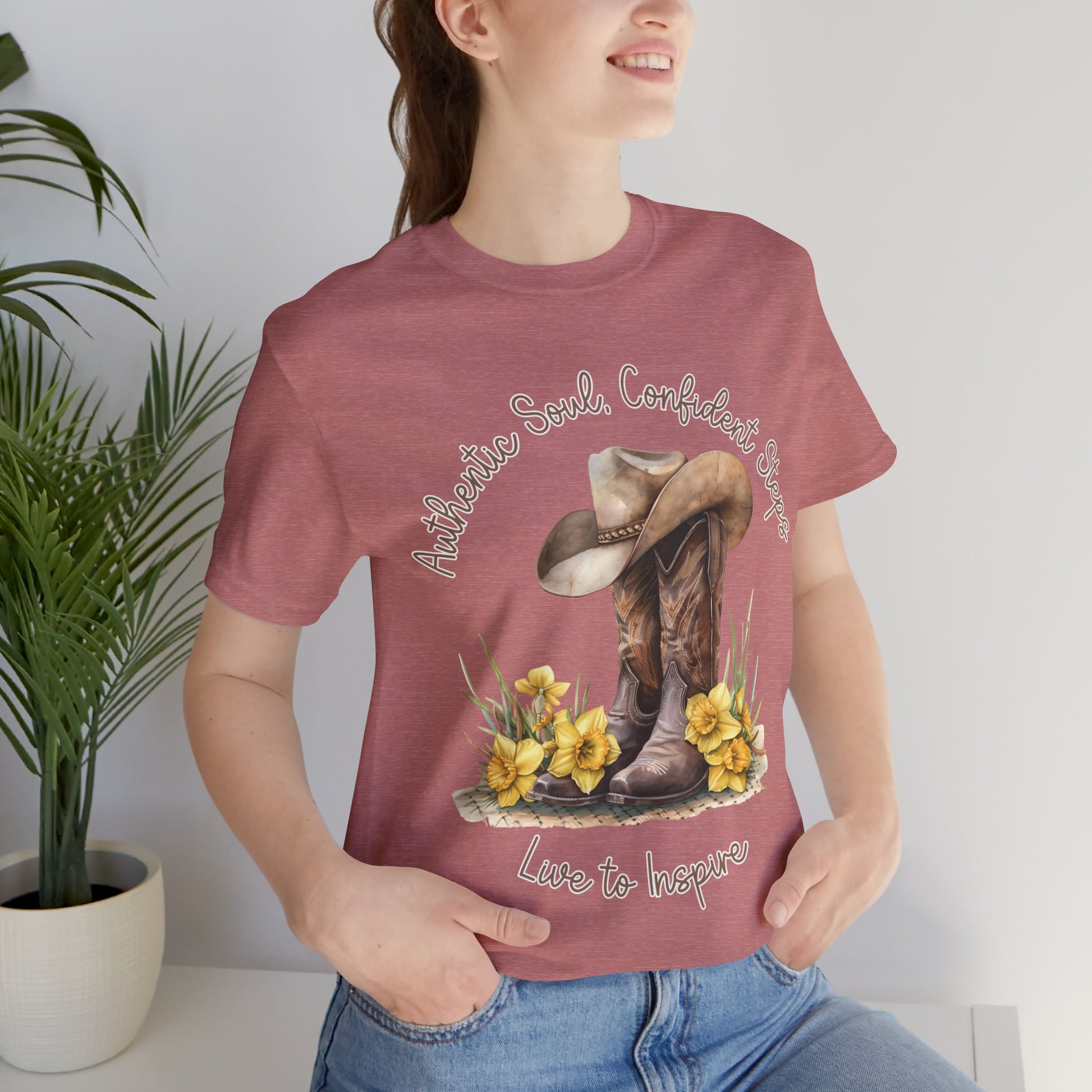 Brown leather cowboy boots with detailed stitching and a light brown hat on top, surrounded by green leaves and yellow flowers, with inspirational phrases ‘Authentic Soul,’ ‘Confident Steps,’ and ‘Live to Inspire’ written above and below on a white background colors tshirt Aqua Athletic Heather Baby Blue Black Dark Grey Heather Heather Kelly Heather Red Heather Team Purple Heather True Royal Navy Pink White Heather Aqua Heather Mauve Charity Pink.