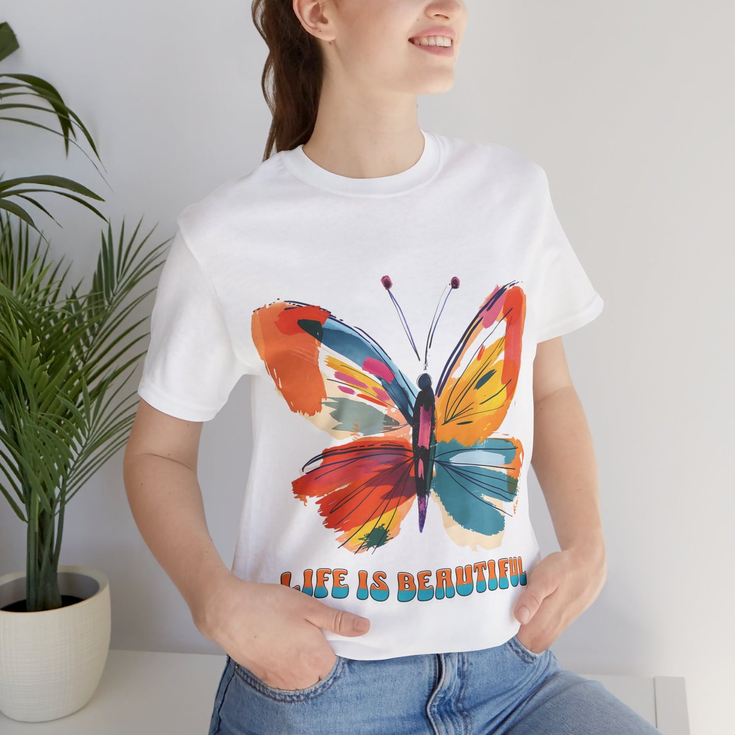 Colorful cartoon-style butterfly with vibrant wings and the text 'Life is Beautiful' designed for t-shirts in colors including Aqua, Athletic Heather, Berry, Black, Dark Grey Heather, Heather Red, Heather Team Purple, Heather True Royal, White, and Charity Pink