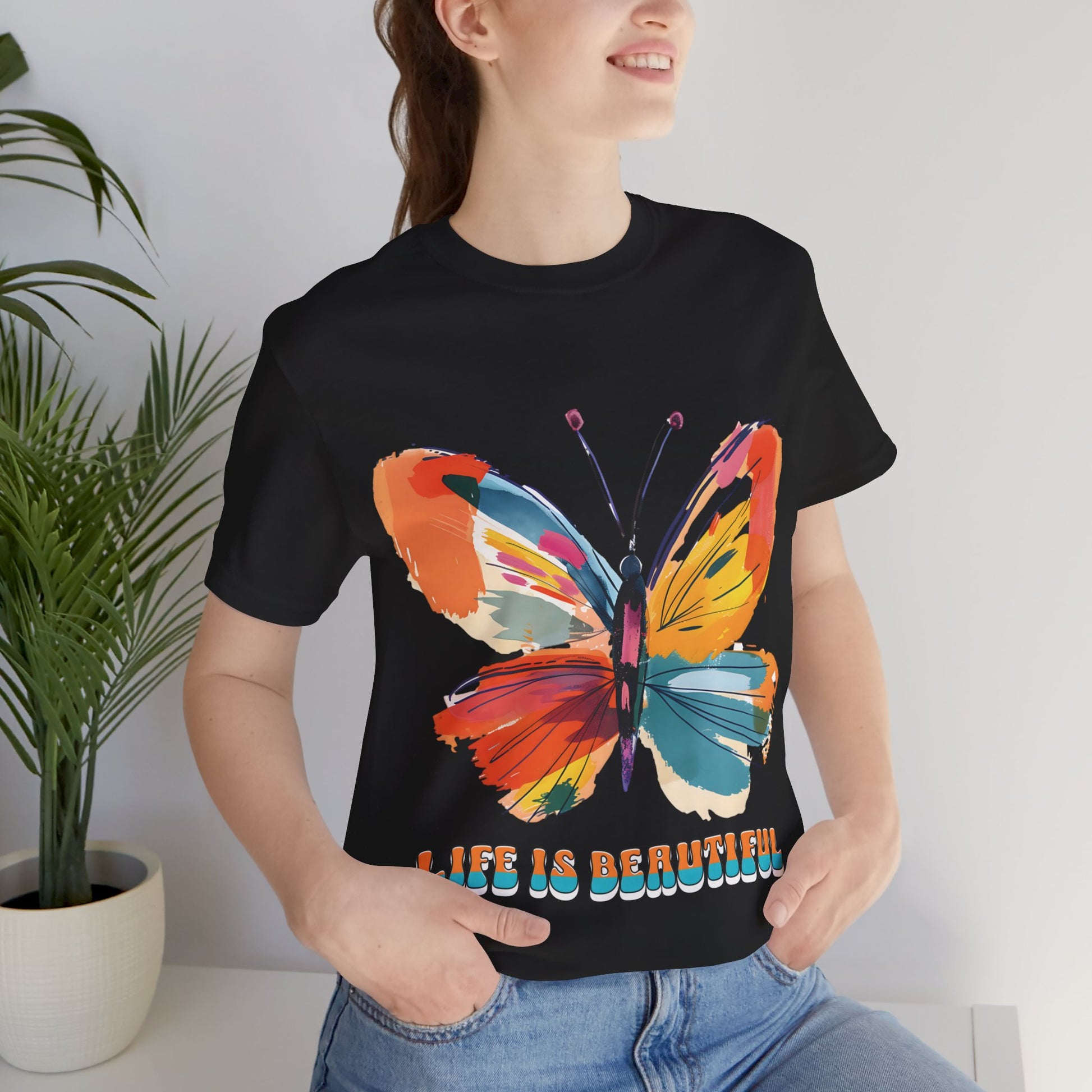 Colorful cartoon-style butterfly with vibrant wings and the text 'Life is Beautiful' designed for t-shirts in colors including Aqua, Athletic Heather, Berry, Black, Dark Grey Heather, Heather Red, Heather Team Purple, Heather True Royal, White, and Charity Pink