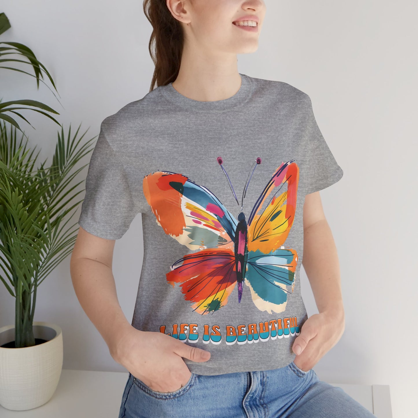 Colorful cartoon-style butterfly with vibrant wings and the text 'Life is Beautiful' designed for t-shirts in colors including Aqua, Athletic Heather, Berry, Black, Dark Grey Heather, Heather Red, Heather Team Purple, Heather True Royal, White, and Charity Pink