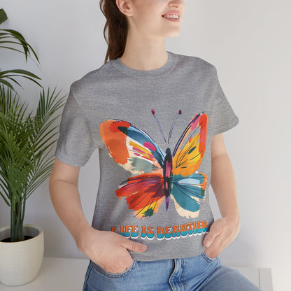 Colorful cartoon-style butterfly with vibrant wings and the text 'Life is Beautiful' designed for t-shirts in colors including Aqua, Athletic Heather, Berry, Black, Dark Grey Heather, Heather Red, Heather Team Purple, Heather True Royal, White, and Charity Pink