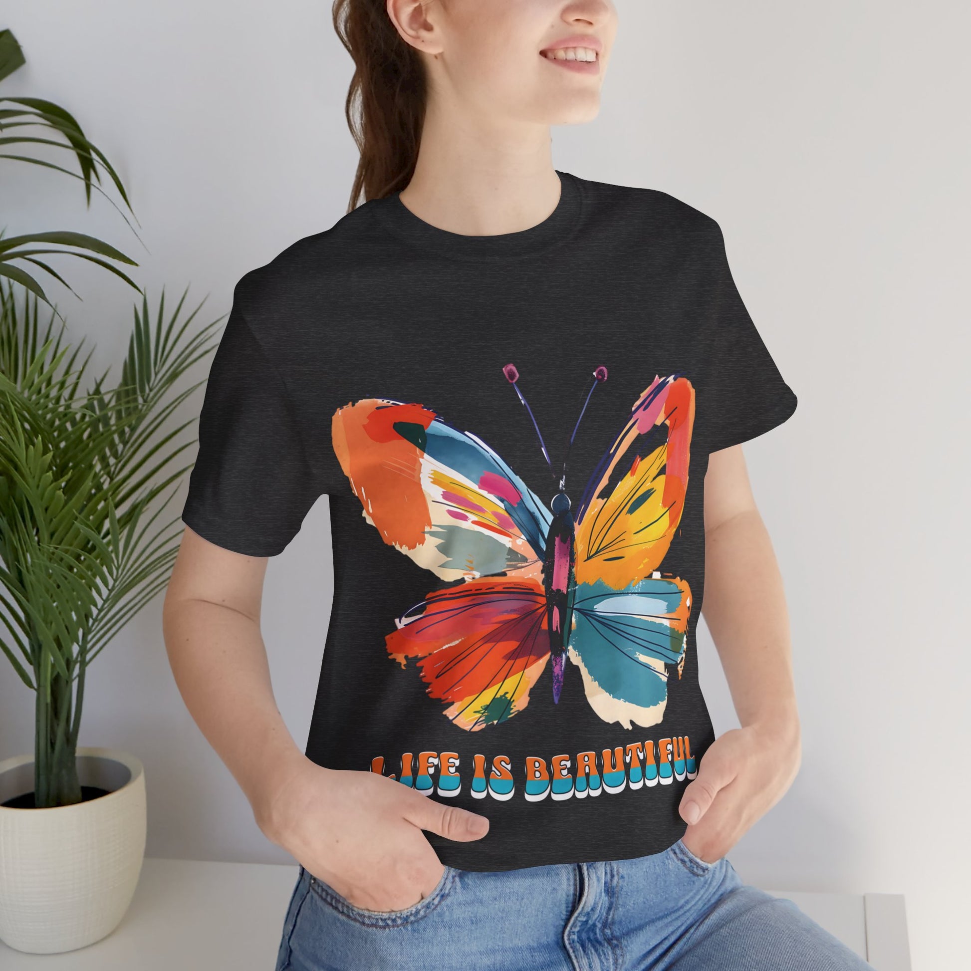 Colorful cartoon-style butterfly with vibrant wings and the text 'Life is Beautiful' designed for t-shirts in colors including Aqua, Athletic Heather, Berry, Black, Dark Grey Heather, Heather Red, Heather Team Purple, Heather True Royal, White, and Charity Pink