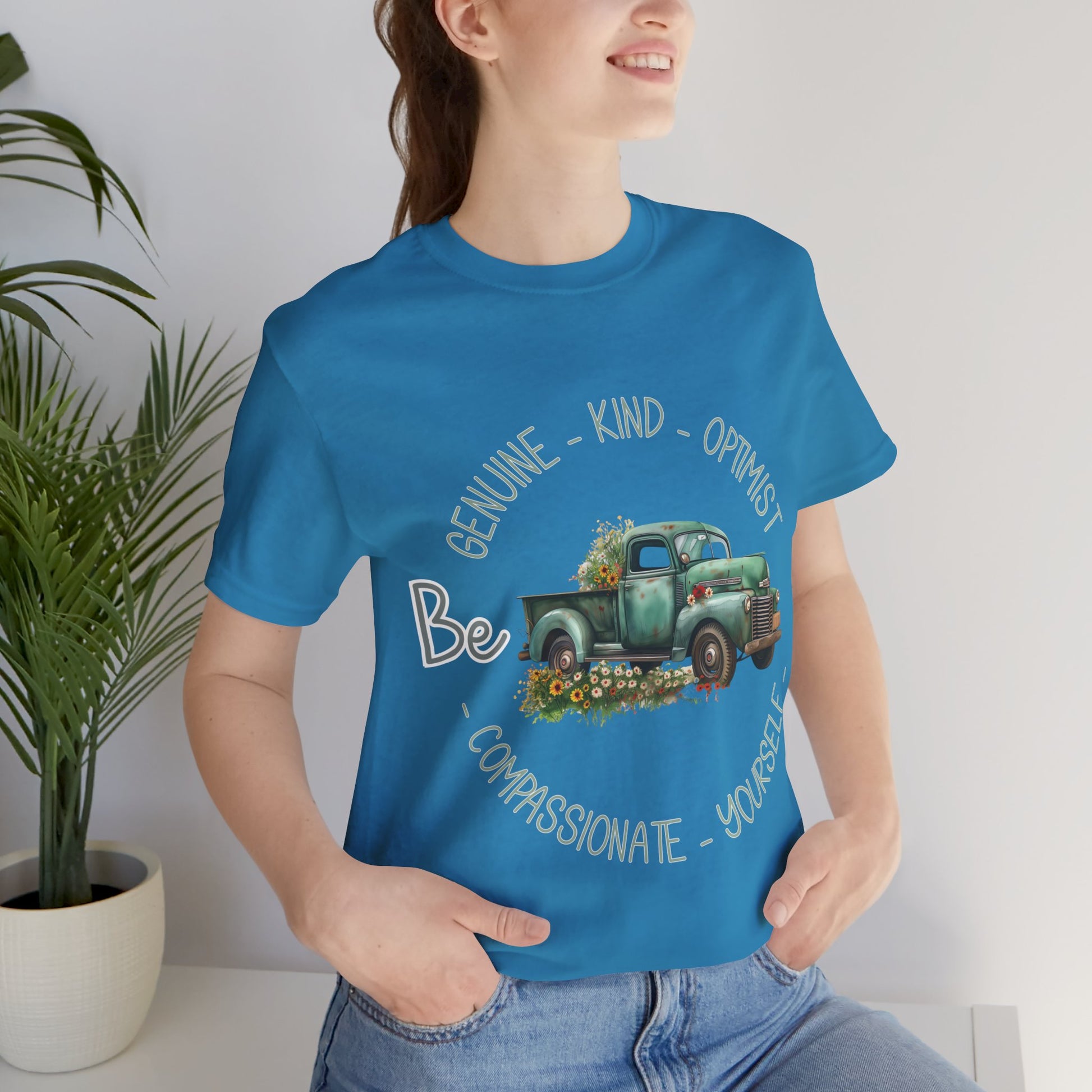 Vintage boho-style illustration of an old green truck surrounded by colorful flowers, with the text 'Be Genuine - Bold - Optimistic - Compassionate - Kind - Yourself.' This design is intended for t-shirts in various colors, including Aqua, Athletic Heather, Black, Dark Grey Heather, Heather Kelly, Heather Navy, Heather Red, Heather True Royal, Kelly, Pink, White, Yellow, Heather Aqua, Heather Ice Blue, Heather Mauve, and Charity Pink.