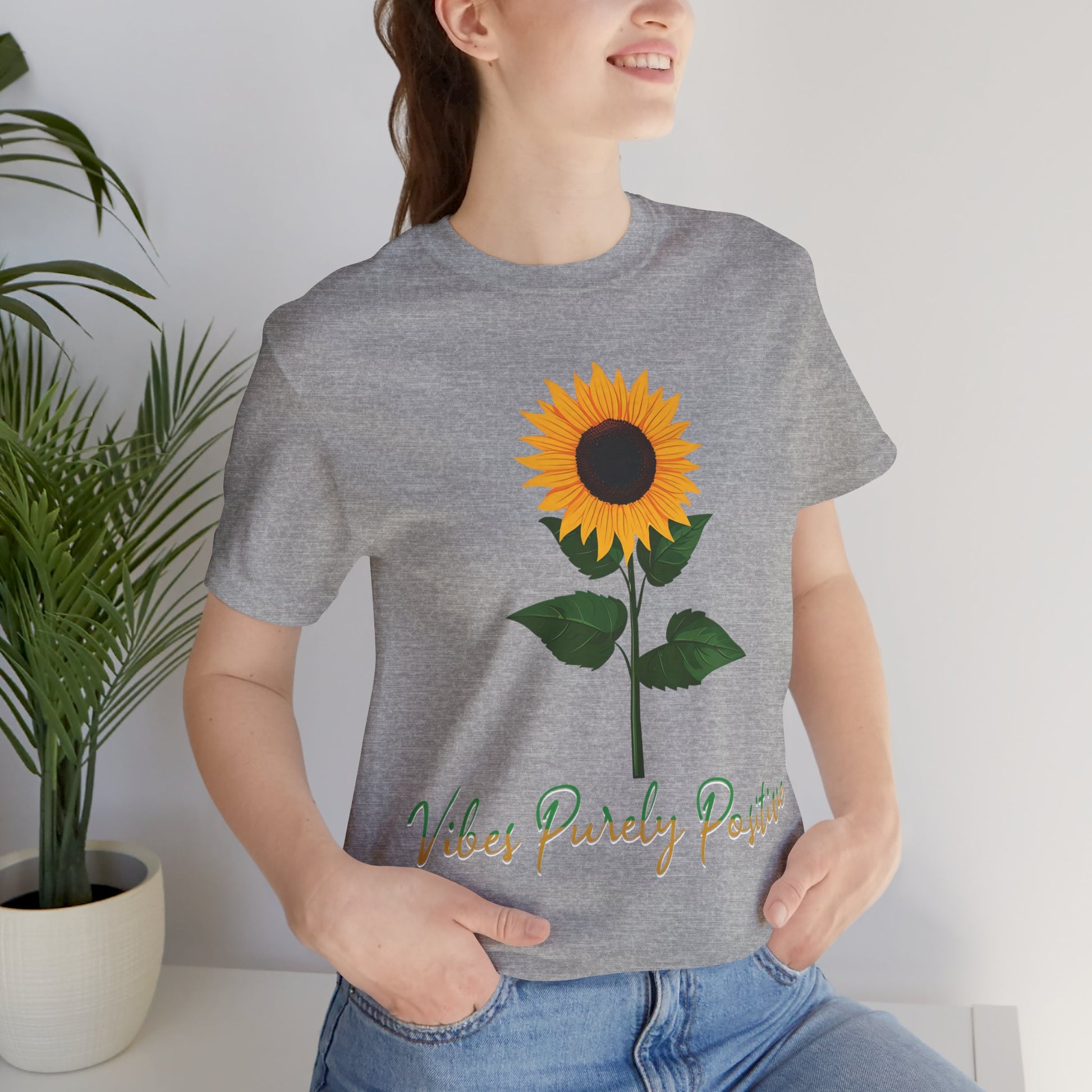 Sunflower illustration with 'Vibes Purely Positive' phrase - a vibrant sunflower with yellow petals and dark brown center, green leaves on a stem, conveying a positive message printed in t-shirts of different colors like "Army Athletic Heather Berry Black Heather Navy Heather Team Purple Navy White Ash Heather Aqua"