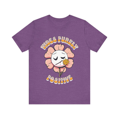 Cute pink flower with a smiling face and a yellow flower in its mouth, accompanied by the text "Vibes Purely Positive." This cheerful design is perfect for t-shirts available in colors Aqua, Berry, Black, Dark Gray, Heather Kelly, Heather Team Purple, Heather True Royal, Navy, White, and Charity Pink.