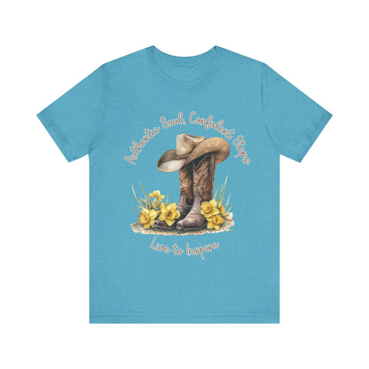 Brown leather cowboy boots with detailed stitching and a light brown hat on top, surrounded by green leaves and yellow flowers, with inspirational phrases ‘Authentic Soul,’ ‘Confident Steps,’ and ‘Live to Inspire’ written above and below on a white background colors tshirt Aqua Athletic Heather Baby Blue Black Dark Grey Heather Heather Kelly Heather Red Heather Team Purple Heather True Royal Navy Pink White Heather Aqua Heather Mauve Charity Pink.