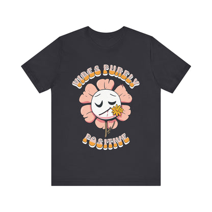 Cute pink flower with a smiling face and a yellow flower in its mouth, accompanied by the text "Vibes Purely Positive." This cheerful design is perfect for t-shirts available in colors Aqua, Berry, Black, Dark Gray, Heather Kelly, Heather Team Purple, Heather True Royal, Navy, White, and Charity Pink.