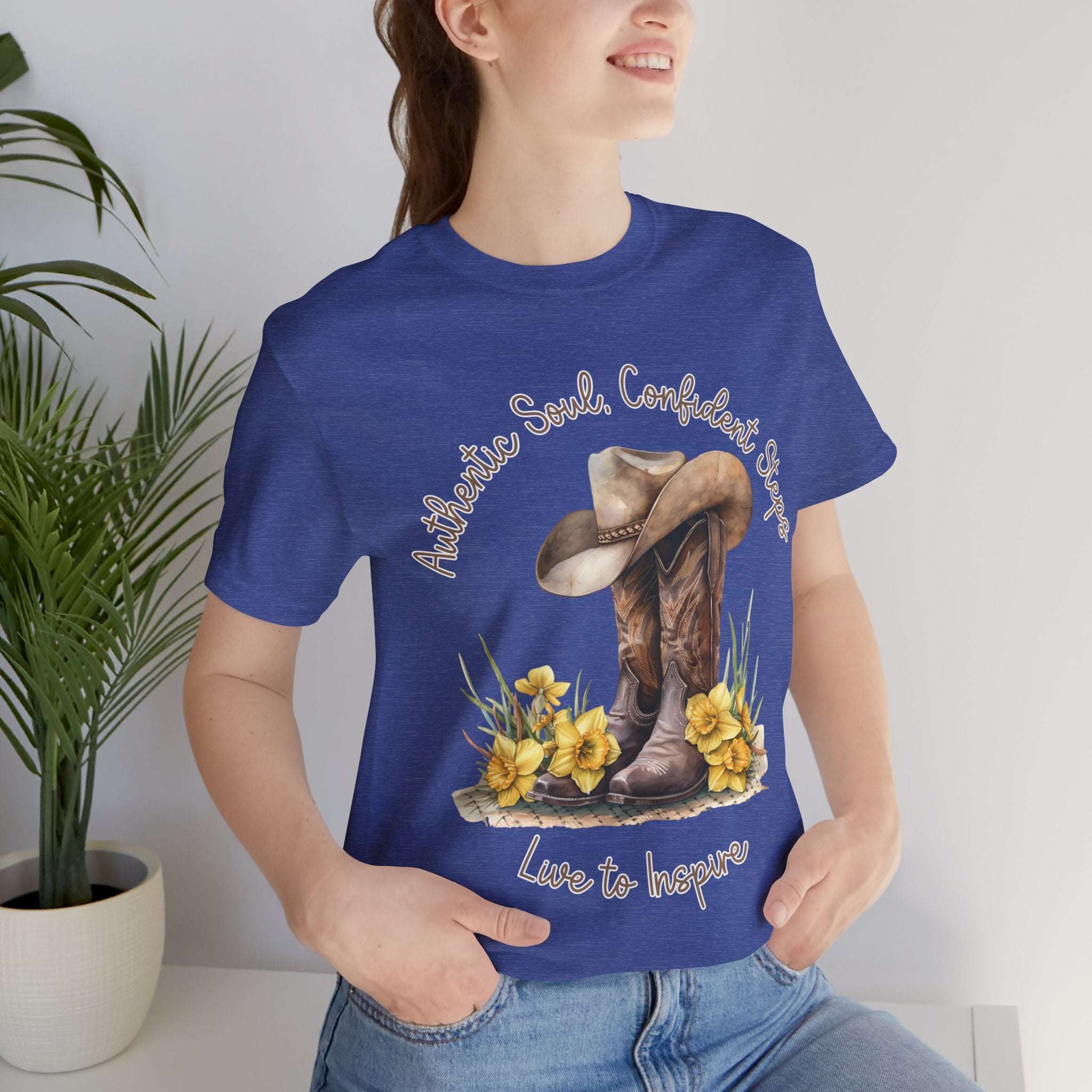 Brown leather cowboy boots with detailed stitching and a light brown hat on top, surrounded by green leaves and yellow flowers, with inspirational phrases ‘Authentic Soul,’ ‘Confident Steps,’ and ‘Live to Inspire’ written above and below on a white background colors tshirt Aqua Athletic Heather Baby Blue Black Dark Grey Heather Heather Kelly Heather Red Heather Team Purple Heather True Royal Navy Pink White Heather Aqua Heather Mauve Charity Pink.