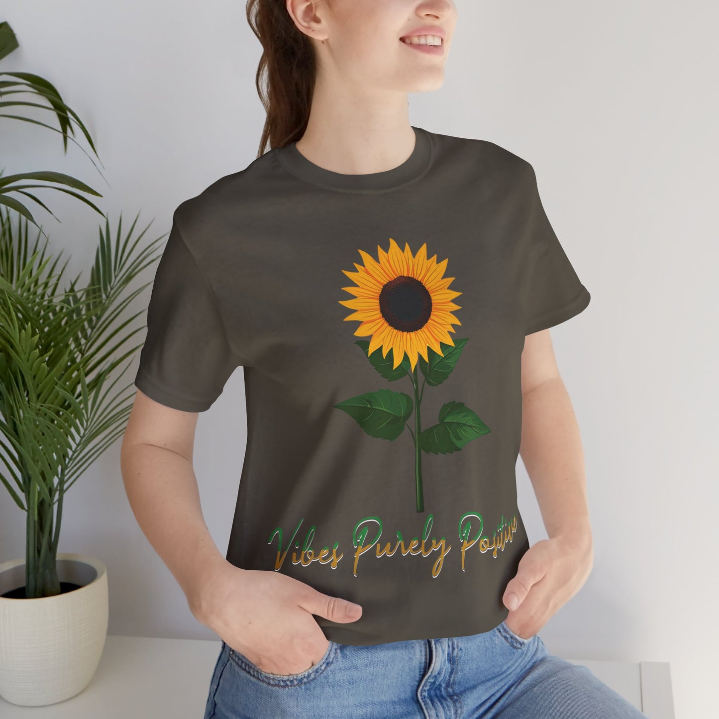 Sunflower illustration with 'Vibes Purely Positive' phrase - a vibrant sunflower with yellow petals and dark brown center, green leaves on a stem, conveying a positive message printed in t-shirts of different colors like "Army Athletic Heather Berry Black Heather Navy Heather Team Purple Navy White Ash Heather Aqua"