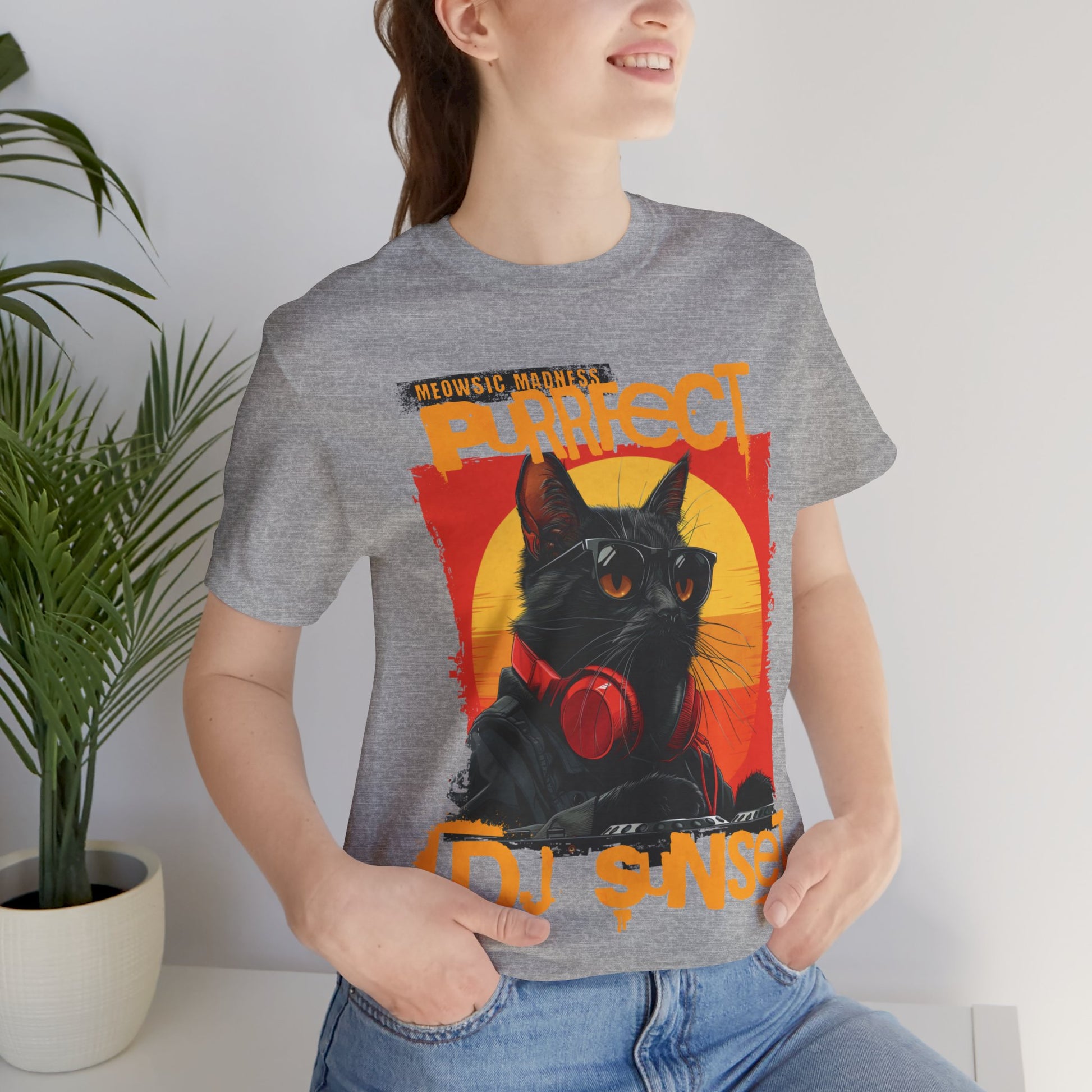 “Turntable Feline: The Sunset DJ Cat – A charismatic black cat dons DJ gear, complete with sunglasses and headphones, set against a vibrant sunset-inspired backdrop, with ‘Meowsic Madness’ and ‘Purrfect’ emblazoned above, capturing the essence of a purrfectly orchestrated music event printed in different t-shirts colors like Athletic Heather Berry Black Dark Grey Heather Heather Navy Navy Ash.” 