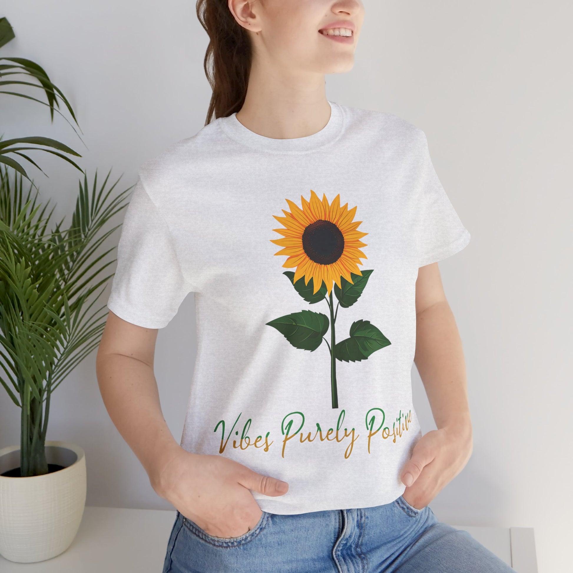 Sunflower illustration with 'Vibes Purely Positive' phrase - a vibrant sunflower with yellow petals and dark brown center, green leaves on a stem, conveying a positive message printed in t-shirts of different colors like "Army Athletic Heather Berry Black Heather Navy Heather Team Purple Navy White Ash Heather Aqua"